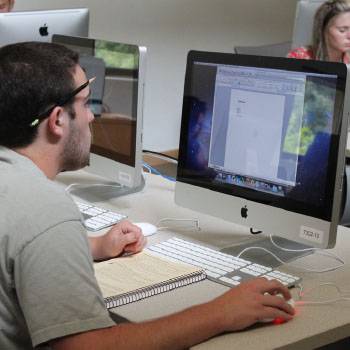 Male student looking at computer with book