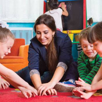 teacher on floor with students hands in middle of circle