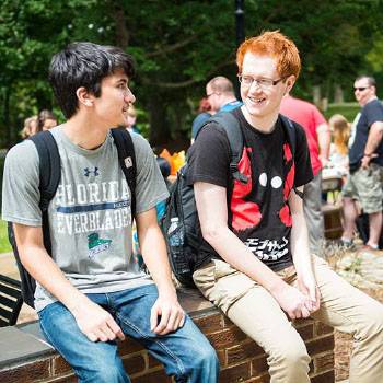 Two male students with backpacks sitting on wall