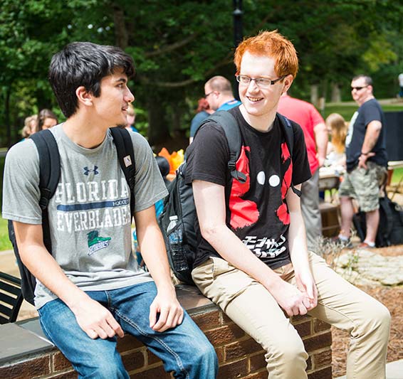 two students with backpack sitting on a short wall