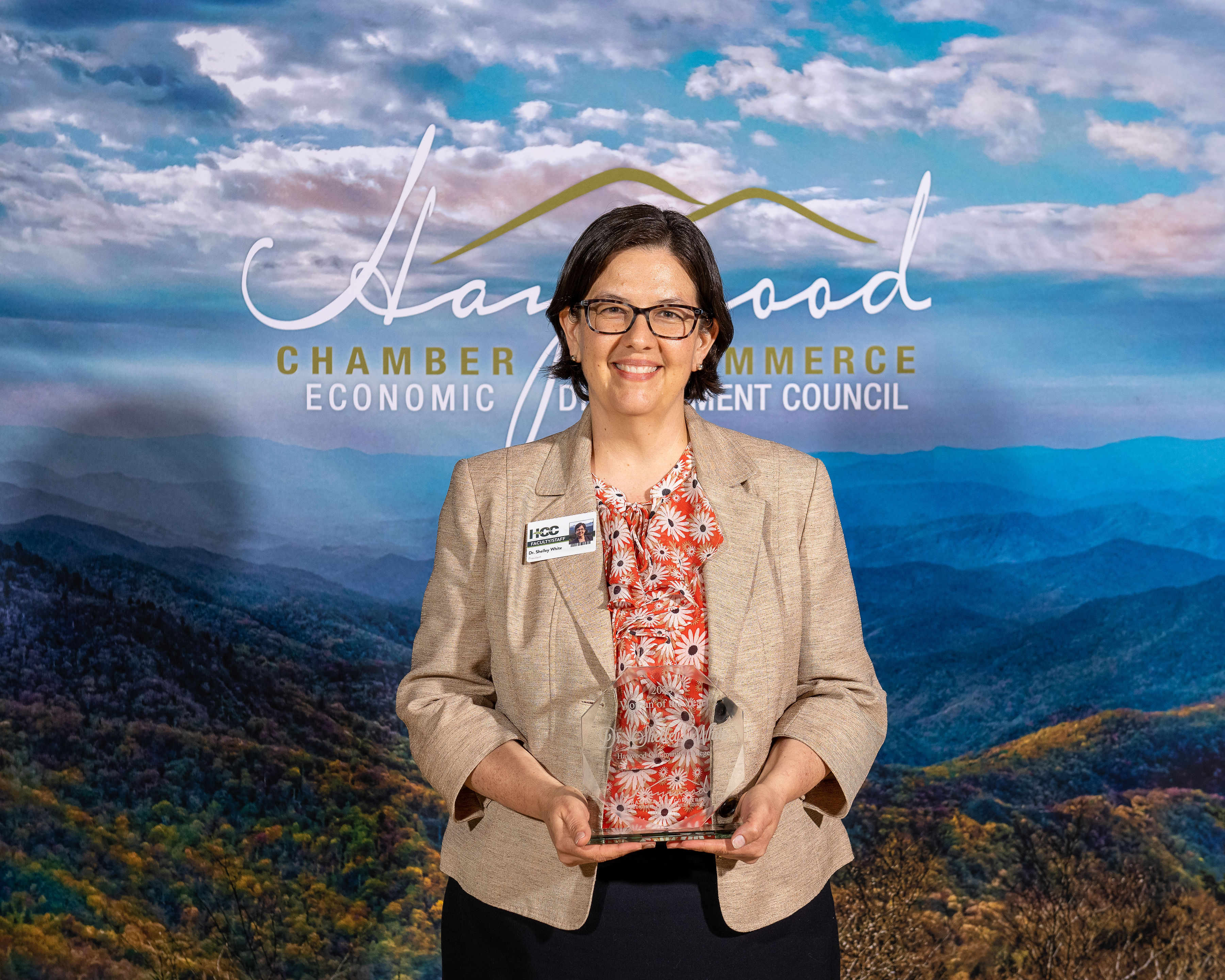 Dr. Shelley White holding award in front of chamber backdrop with mountains