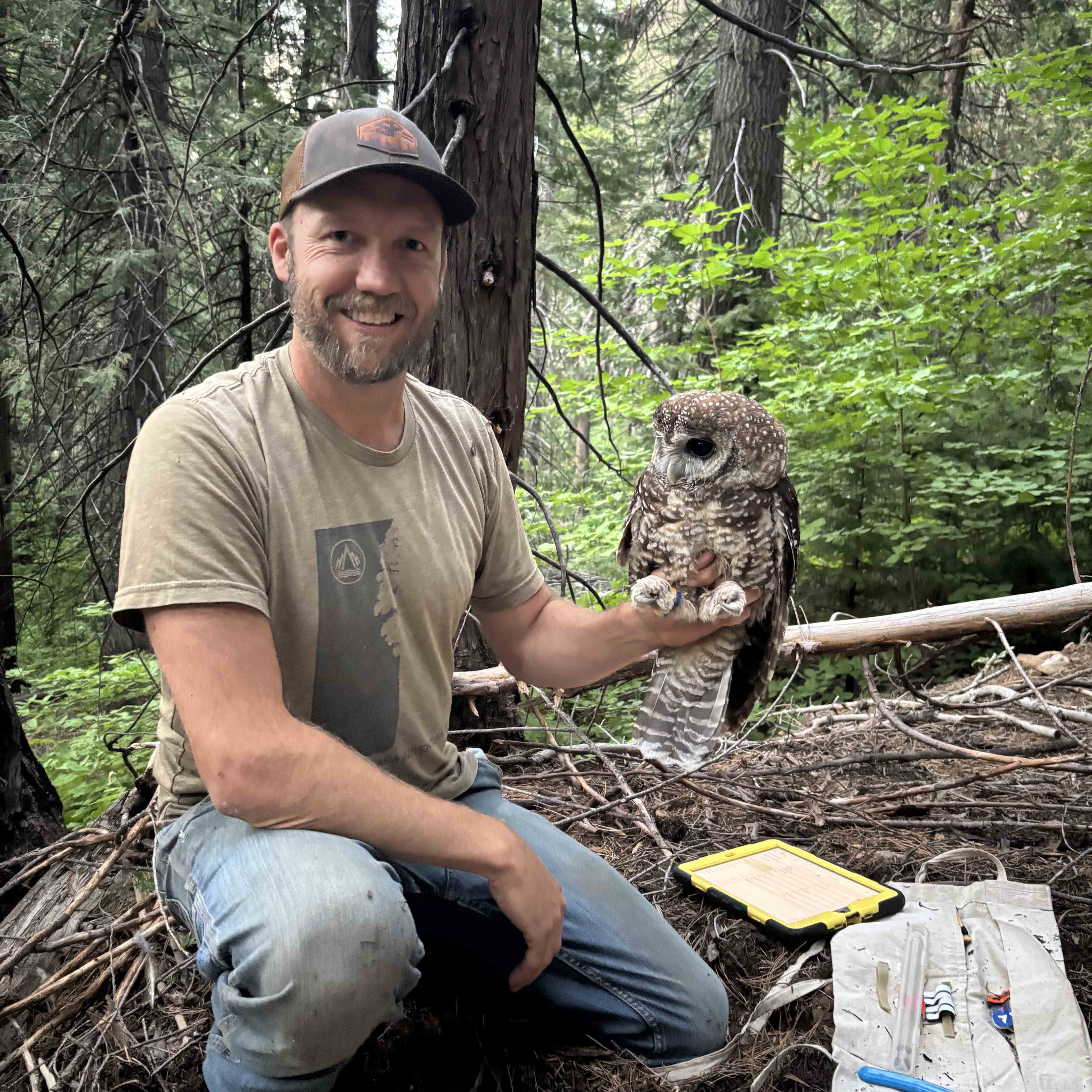 Matthew Andrews squatting down in a forest with an owl perched on his hand