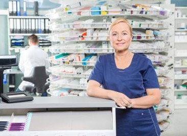 woman pharmacy technician by counter with medications in the background