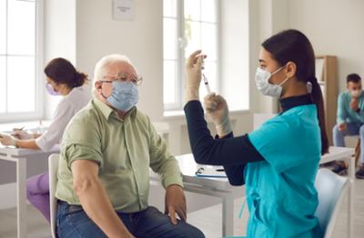 nurse preparing shot for older masked male