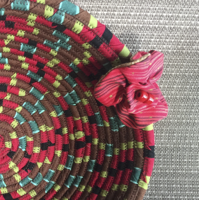 A detail photography of a red, black, and yellow ball that has been made by coiling cotton in a have sphere, using fabric for color.