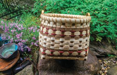 handmade woven basket with small handles on the top in two shades of brown in a garden