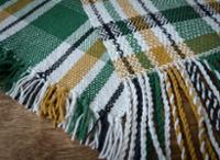 Woven cloth project with a patter including white, green, gold, and black yarn sitting on a woden table.