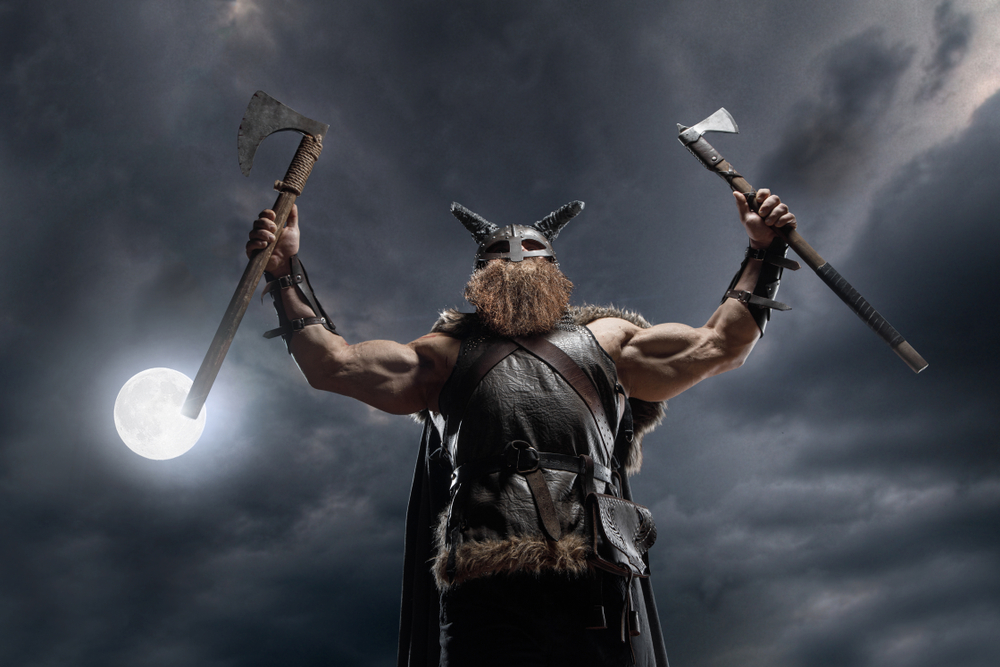 A heroic figure with axes wearing a viking like helmet and armour.