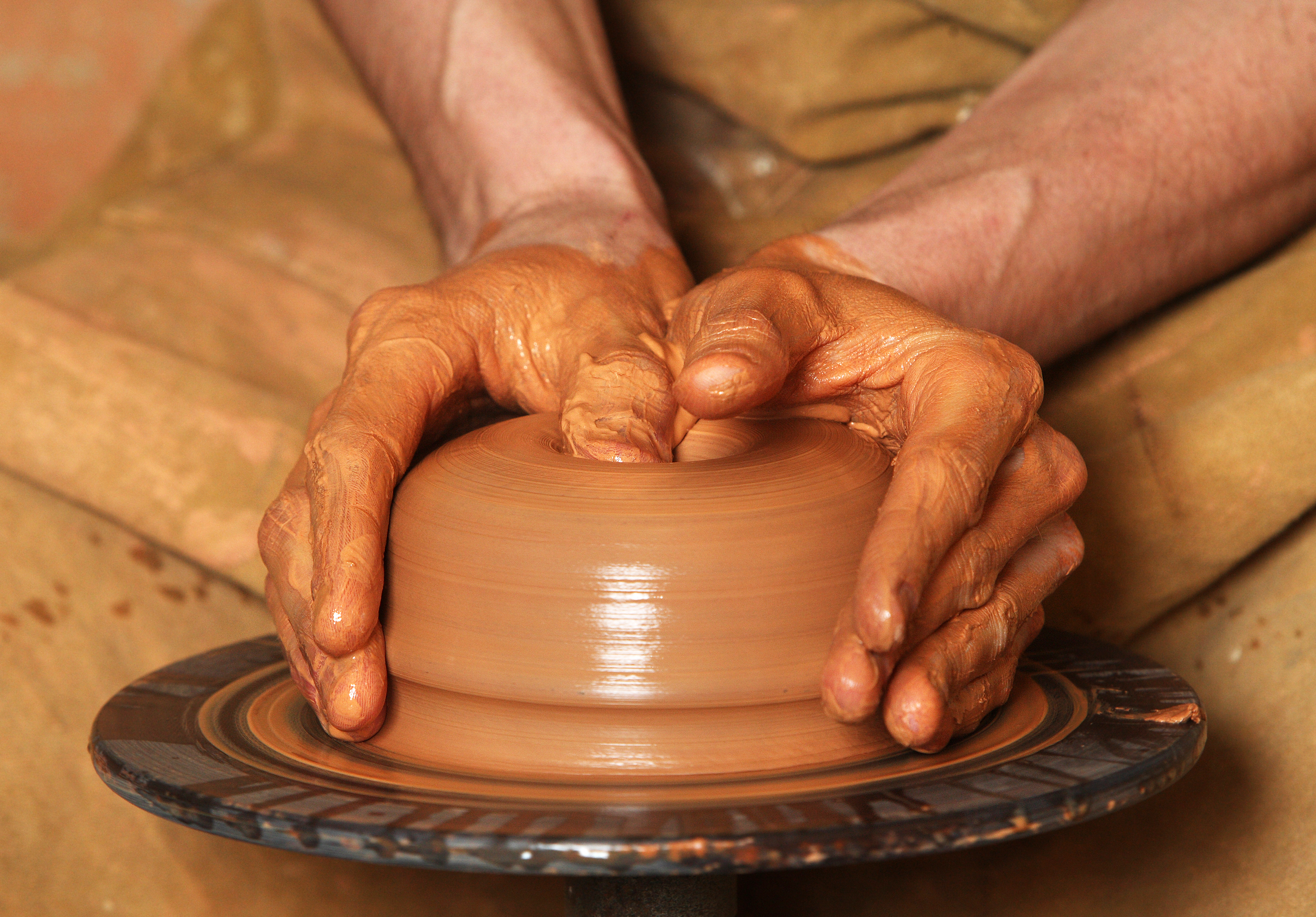 A photography of a turning clay into a bowl using a spinning wheel.