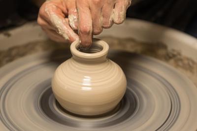 Hands and Fingers are shaping a small vase out of clay on a spinning wheel.