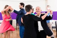 Three couples dancing in a large room with their arms raised