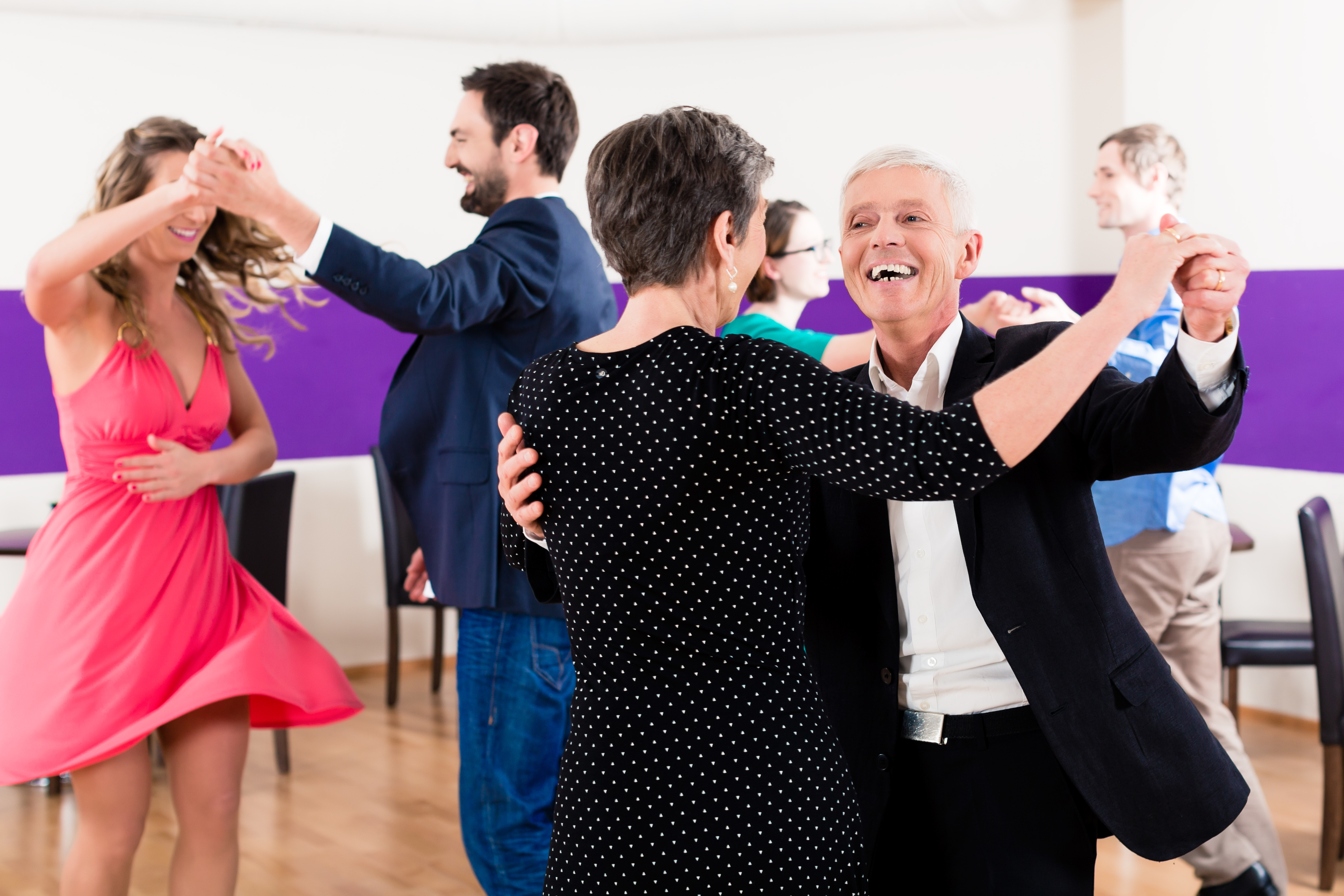 three couples dancing in a large room holding hands up high