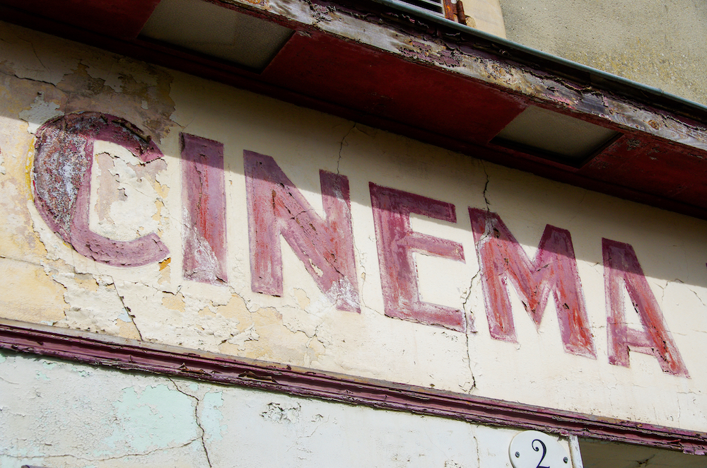 A vintage sign of the word "Cinema" painted with red paint against a white background.