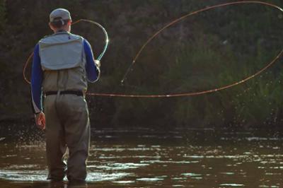 A man fishing for salmon, casting his fly rod into a lake in a natural setting.