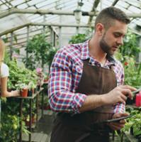 man in greenhouse with plants using a clipboard and pen to exaime plants