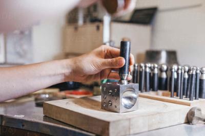 Detail photography of hands using a jewelry tool to bend metal.