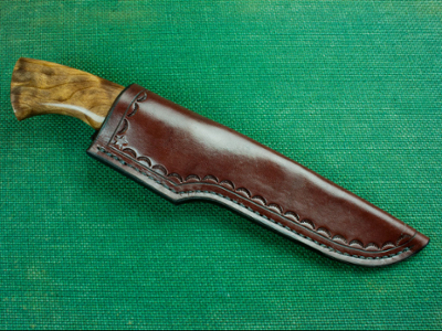 An example of what is made in the course; a leather hand sewn knife covering against a green background. Knife is included in image.