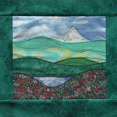 A landscape picture made with pieces of fabric. Landscape is of a mountain view.