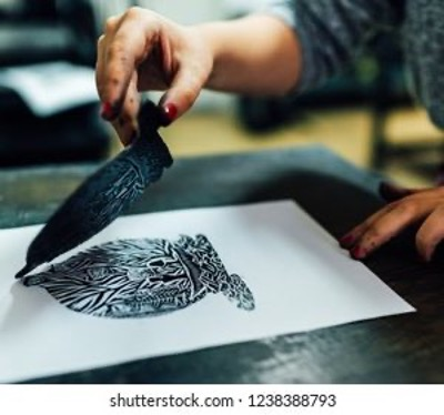A form of printmaking is being done using a lenolium cut stamp and black ink on a white peice of paper. 