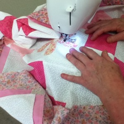 Hands taking a quilt and running it through a sewing machine.