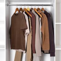 **Alt text:**   Open wardrobe with a capsule-style clothing collection hanging on wooden hangers from a metal closet rod. The garments include neutral-toned T-shirts, sweaters, pants, and a sweatshirt in shades of brown, beige, cream, and dark gray. The clothing is neatly arranged inside a white closet, emphasizing a coordinated, minimalist wardrobe.