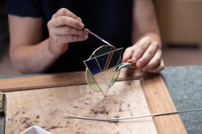 student with small piece of stained glass using small paintbrush