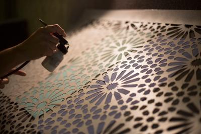 An artist spraying a stencil design with a paint sprayer.