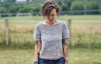 woman with field behind her wearing a gray knitted sweater