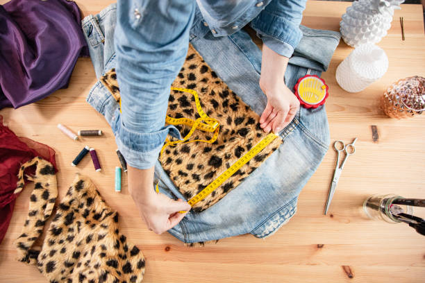 A woman is measuring a cheeta print to fit the back of her jean jacket, to create a rock look for the wild soul.