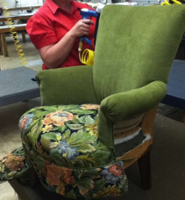 green wing back chair with student using a staple gun on back to attach fabric