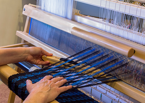 Woman weaving a blue and black scarf using a floor loom.