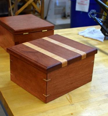 Small Wooden box made of two different types of wood that is hinged with wooden pieces on the sides.