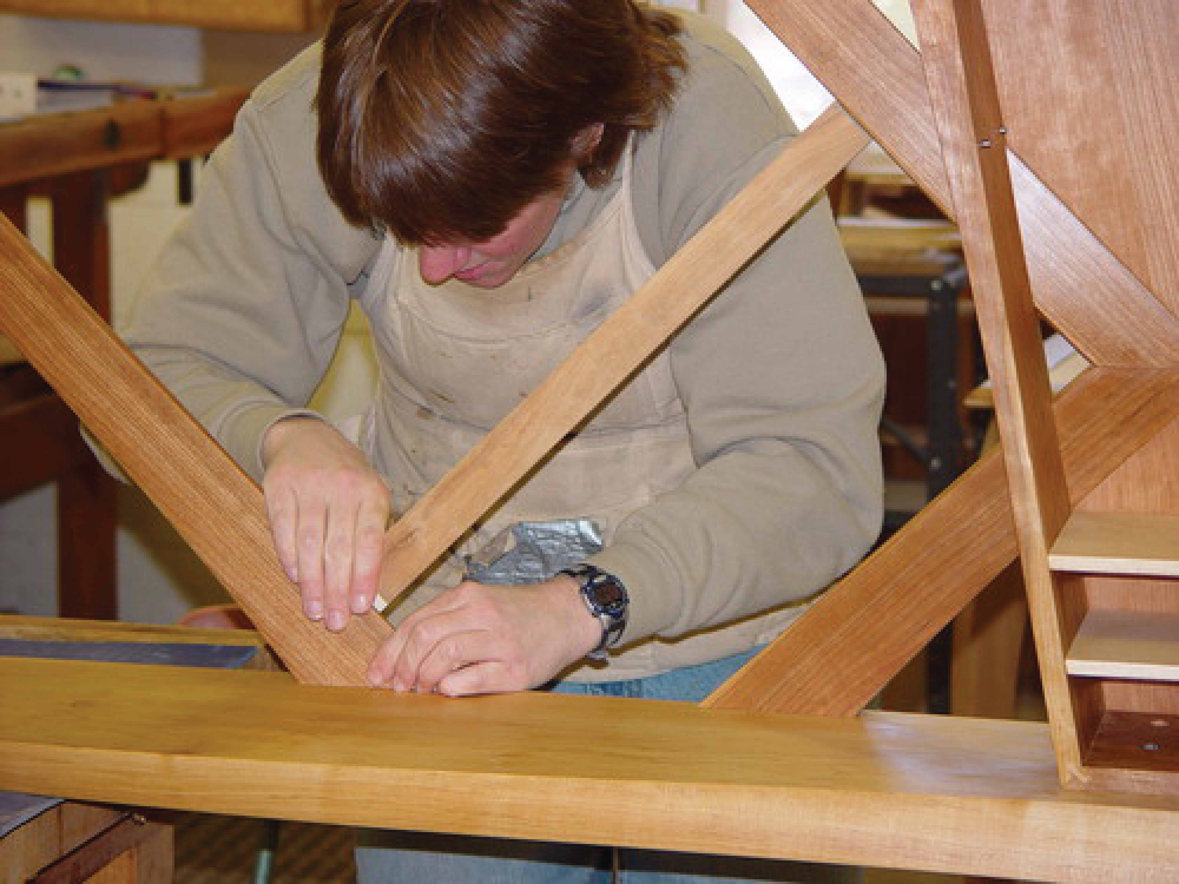 A young man working on the legs of a table in a wooodshop.