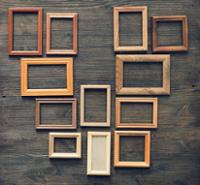 Collection of eleven empty wooden picture frames in various sizes and rectangular orientations arranged on a dark wood tabletop. The frames have different natural wood tones, ranging from light beige to medium and dark brown, and are spaced in an organized pattern across the textured wood-grain background.