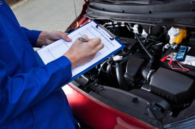 man with clipboard and open car hood looking at engine