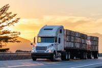 large truck carrying containers on mountain road with sunset in background