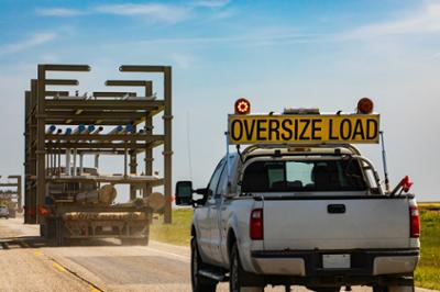 white pickup truck with oversize load sign behind large truck bed with oversize load