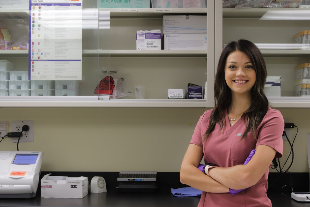 medical student in scrubs next to counter and medical storage