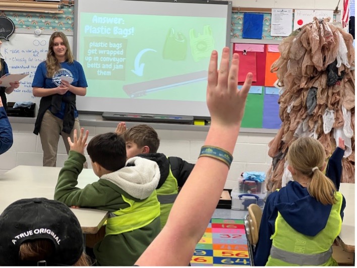 Paige East presenting in classroom with students and bag monster costume on the right