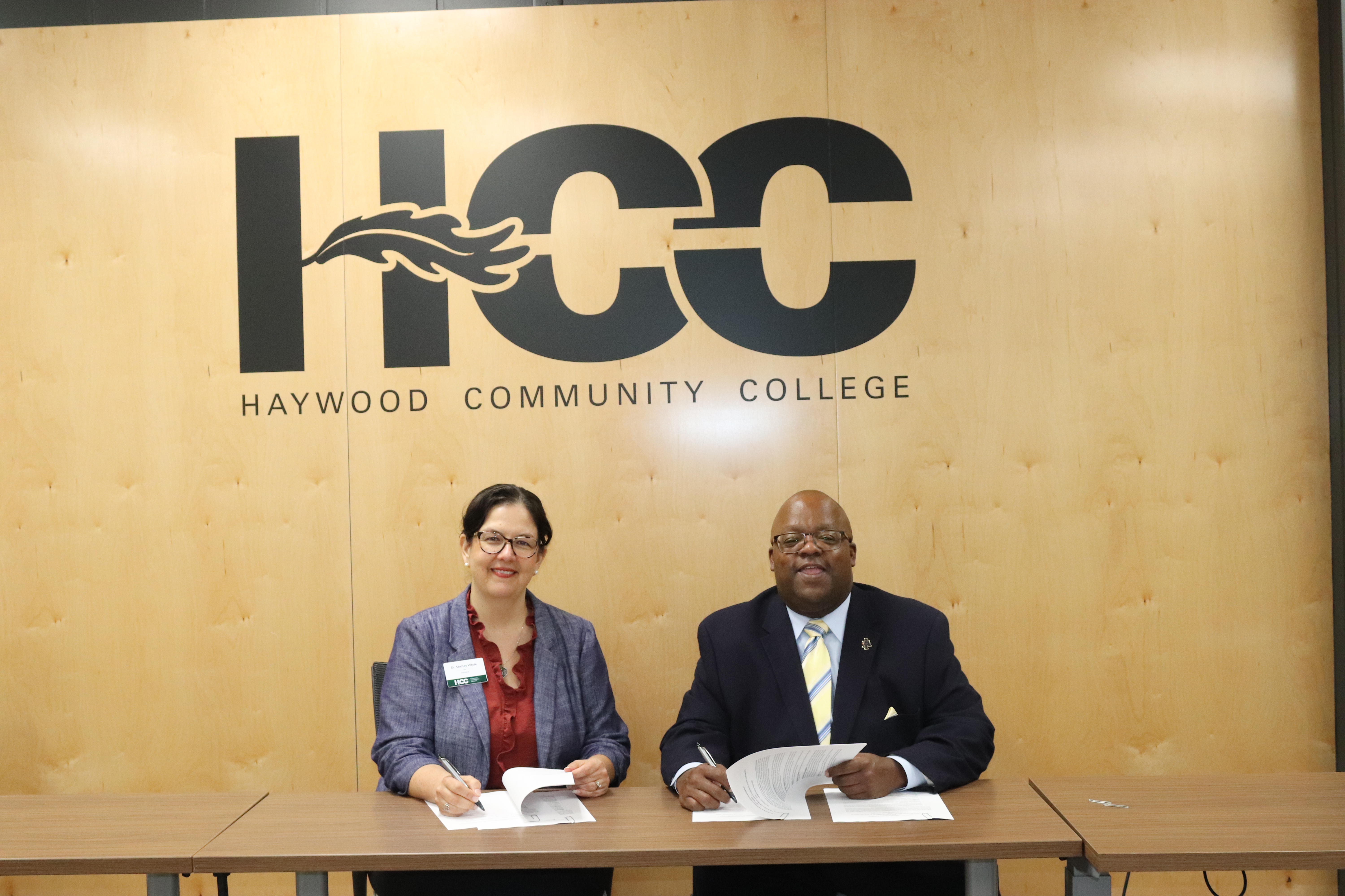 Dr. Shelley White and Dr. Antoine Alston smiling to camera signing papers