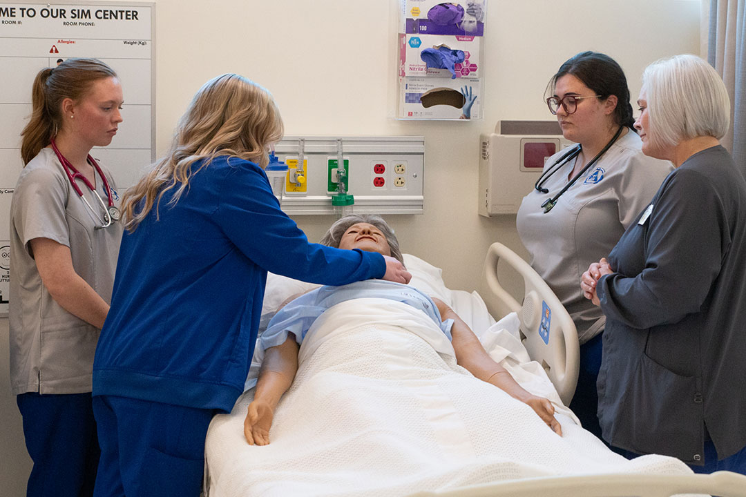 A group of nursing students receive instruction while using a medical mannequin.