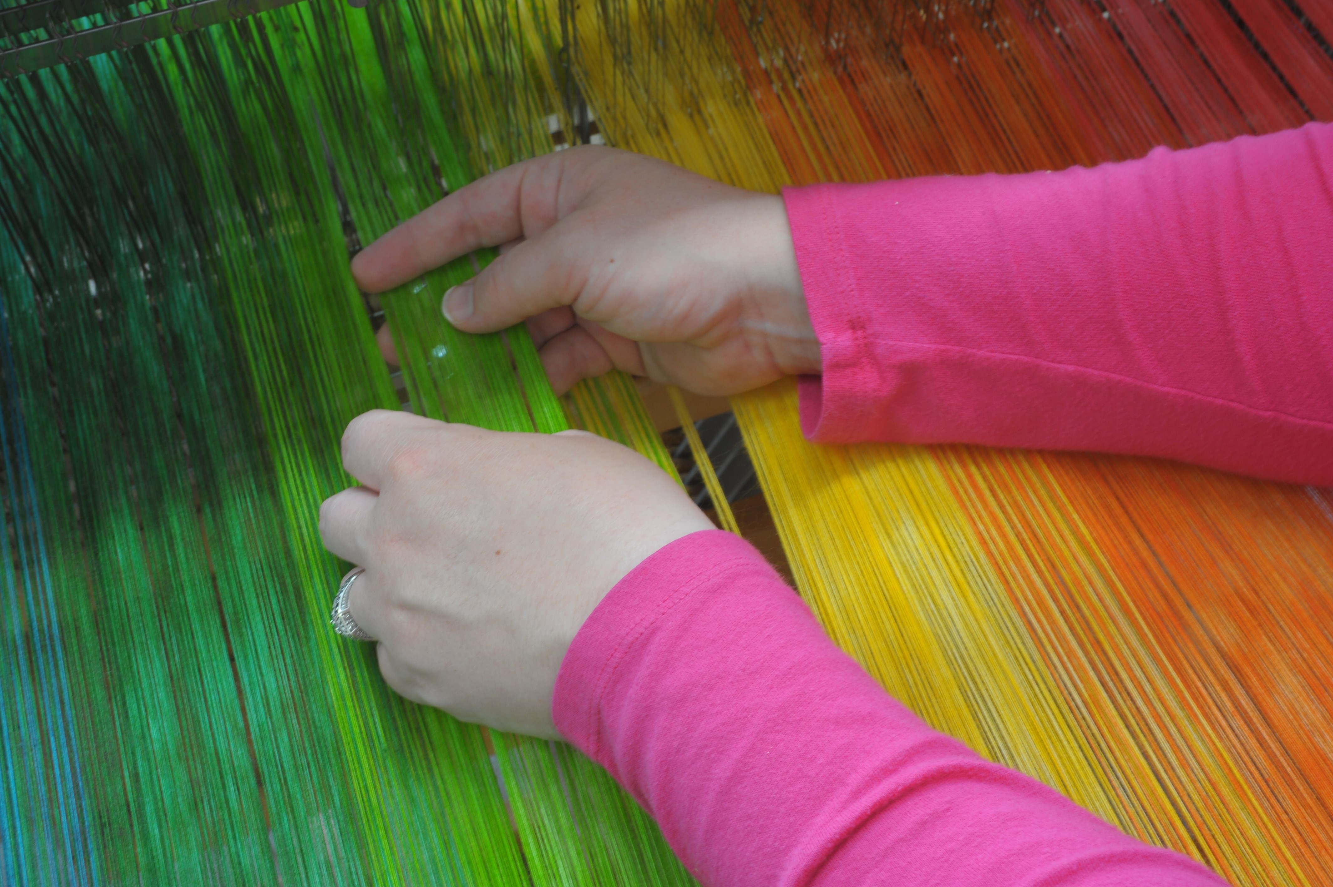 rainbow thread on loom with hands working for weaving