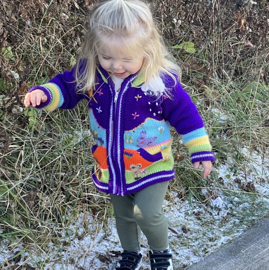 little girl with blonde hair on sidewalk with purple sweater on